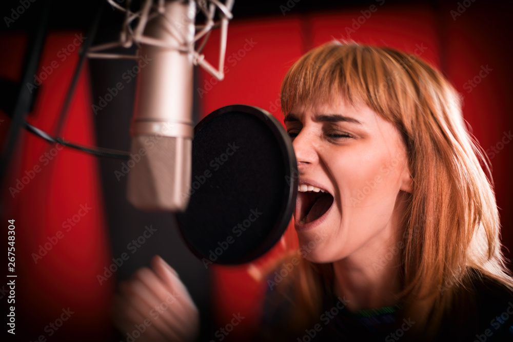 Female singer with microphone recording a song in music studio