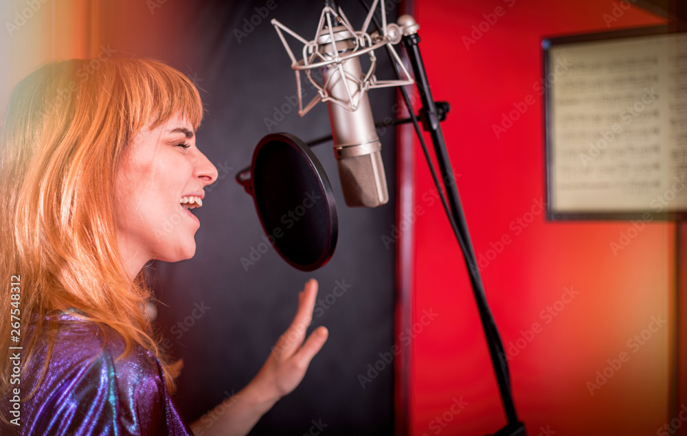 Female singer with microphone recording a song in music studio