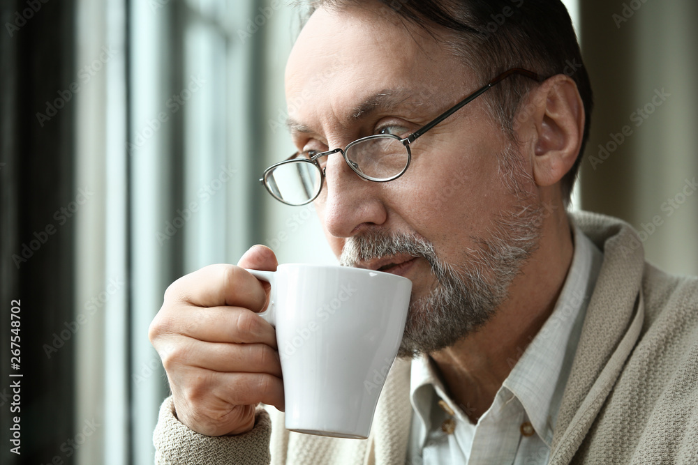 Handsome mature man drinking coffee near window