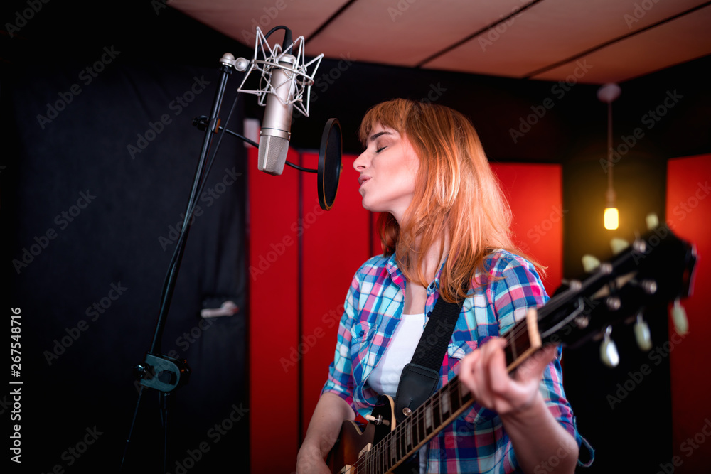 Female singer with electric guitar recording a song in studio