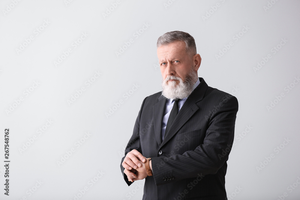 Handsome mature businessman looking at watch on light background