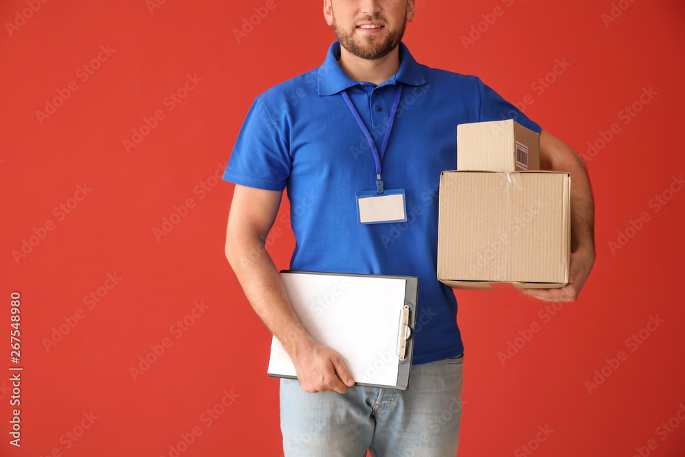 Handsome delivery man with boxes and clipboard on color background