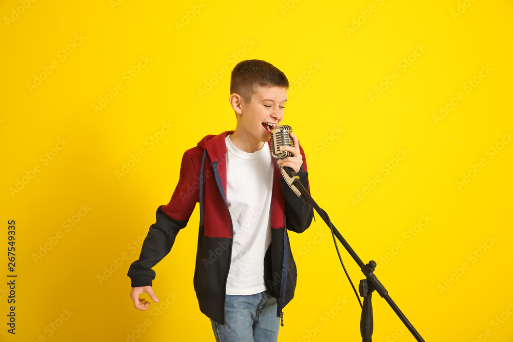 Teenage boy with microphone singing against color background