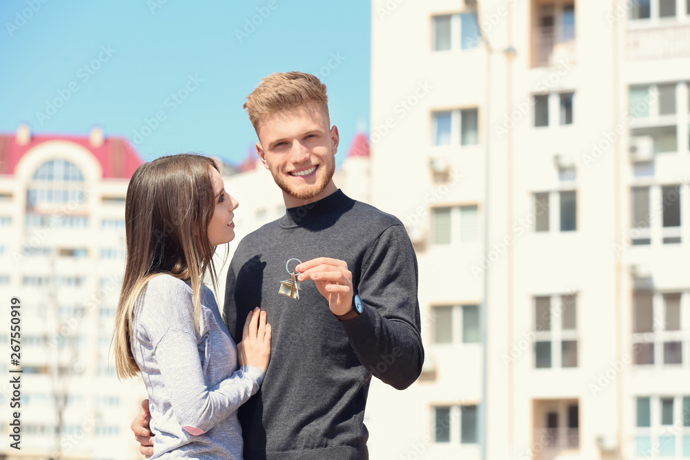 一对年轻夫妇带着钥匙在户外新房子附近