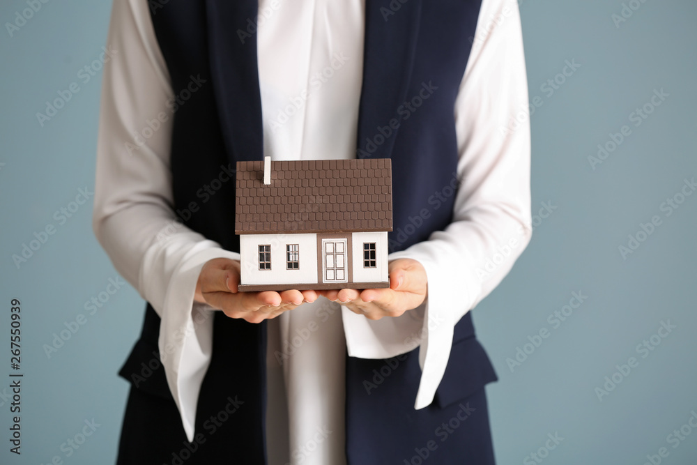 Female real estate agent with house model on grey background, closeup