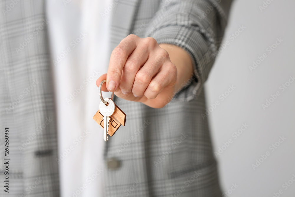 Female real estate agent with key on grey background, closeup