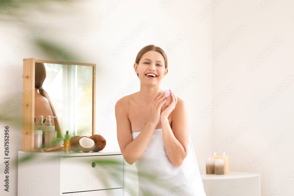 Beautiful young woman applying cream with coconut extract at home