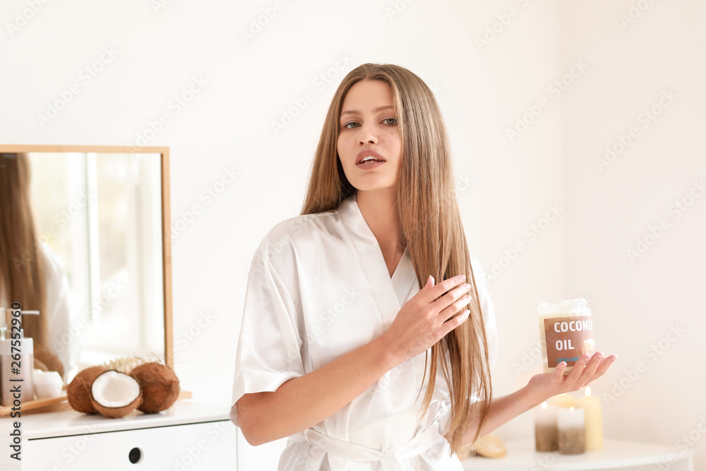 Beautiful young woman applying coconut oil on hair at home