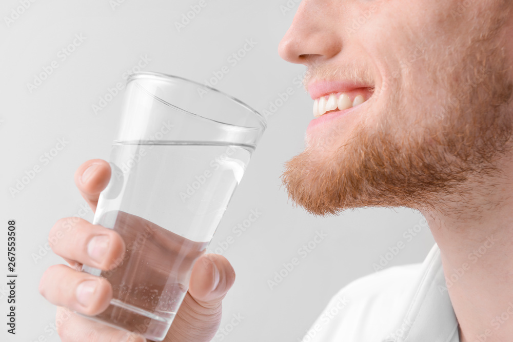 Man with glass of fresh water on light background, closeup