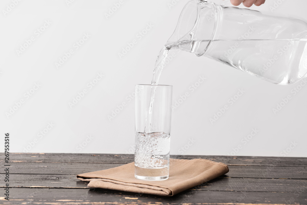 Pouring of fresh water into glass on table