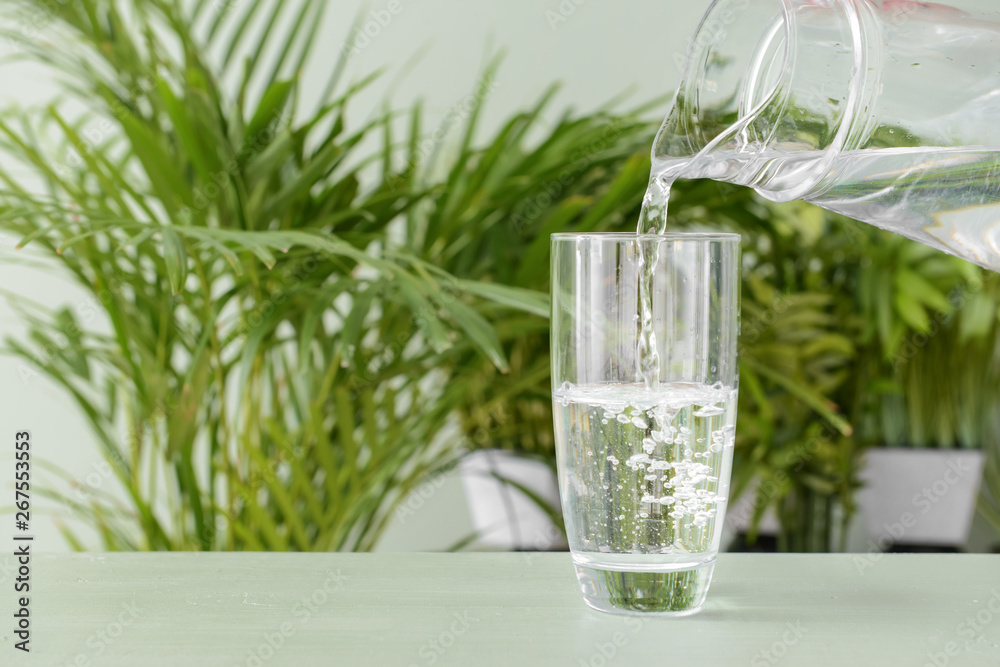 Pouring of fresh water into glass on table