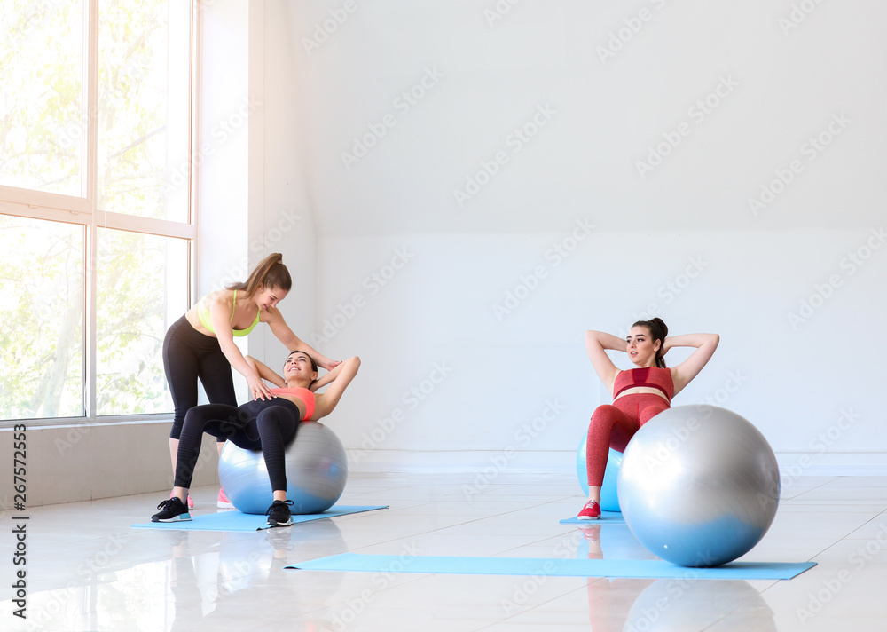 Young sporty women with fitballs doing exercises under supervision of trainer in gym