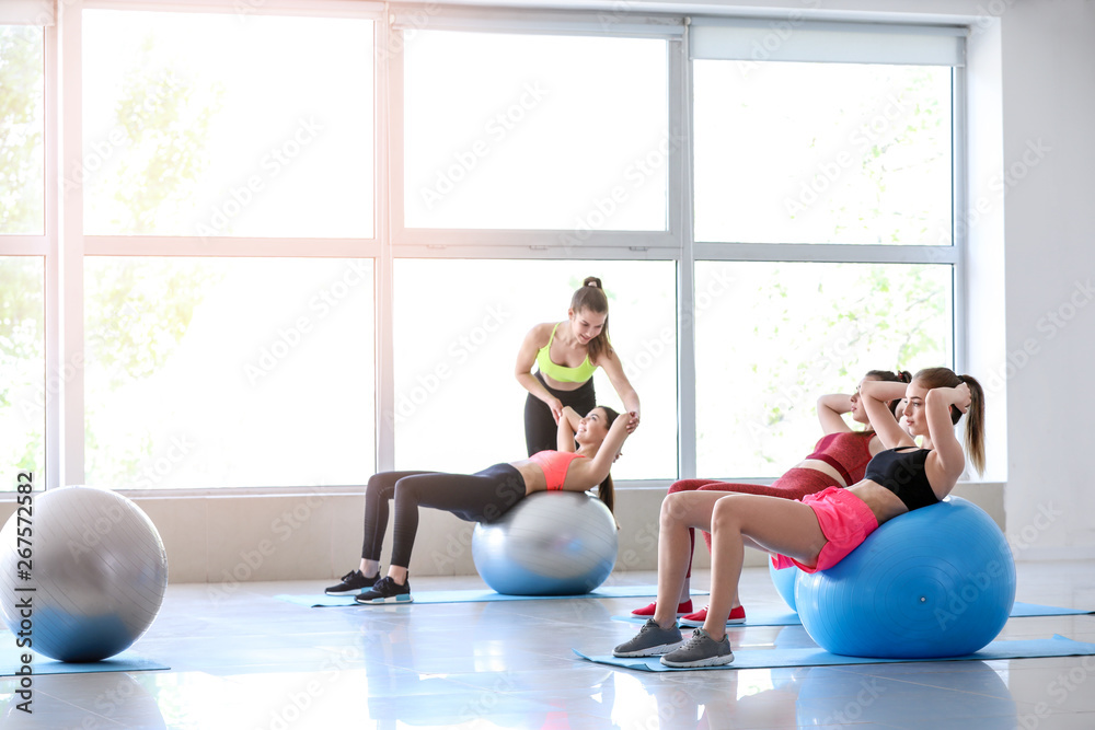 Young sporty women with fitballs doing exercises under supervision of trainer in gym