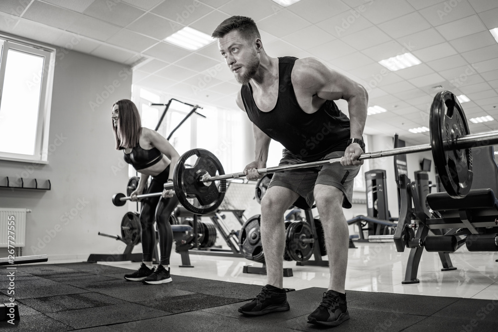 Strong man lifting heavy barbell looking focused in the gym. Muscular man and beautiful woman doing 