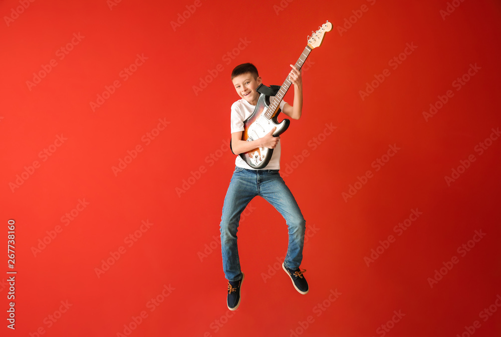 Teenage boy playing guitar against color wall