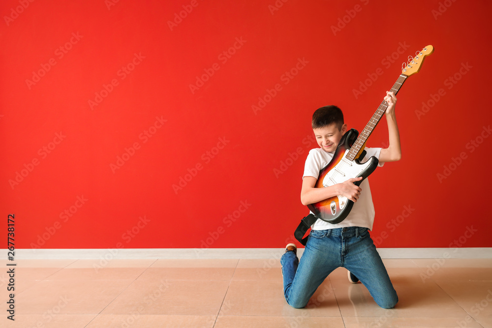 Teenage boy playing guitar against color wall