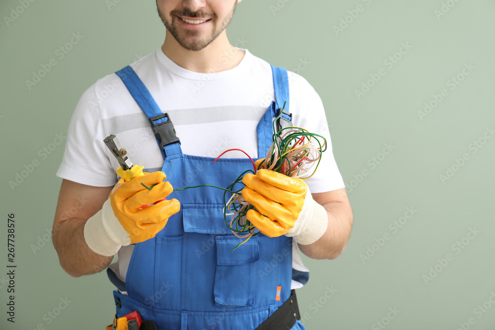 Male electrician with wires and tool on color background, closeup