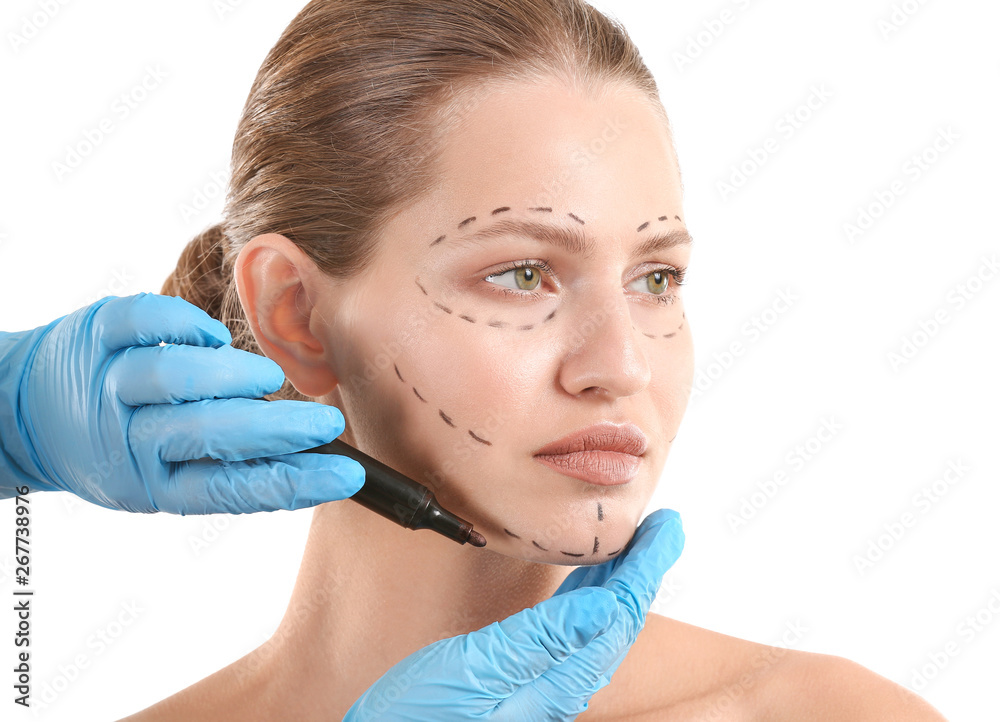 Plastic surgeon applying marking on female face against white background