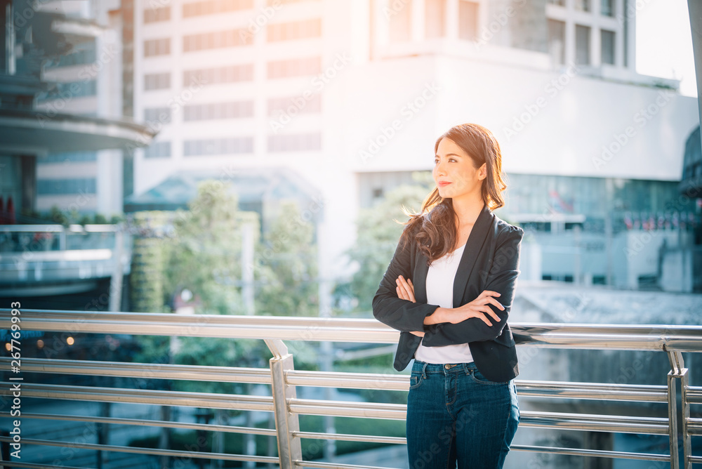 Portrait of a smiling asian businesswoman standing with arms folded on blurred city background. Busi