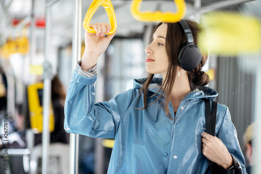 Young stylish woman enjoying trip in the public transport, standing with headphone while moving in t