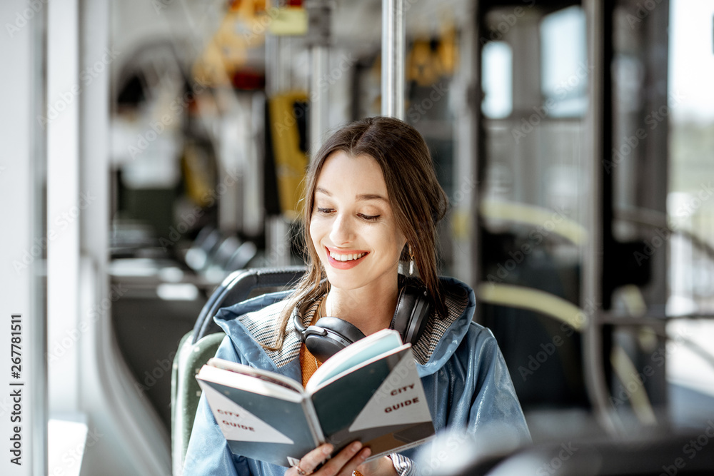 Young woman reading book while moving in the modern tram, happy passenger at the public transport