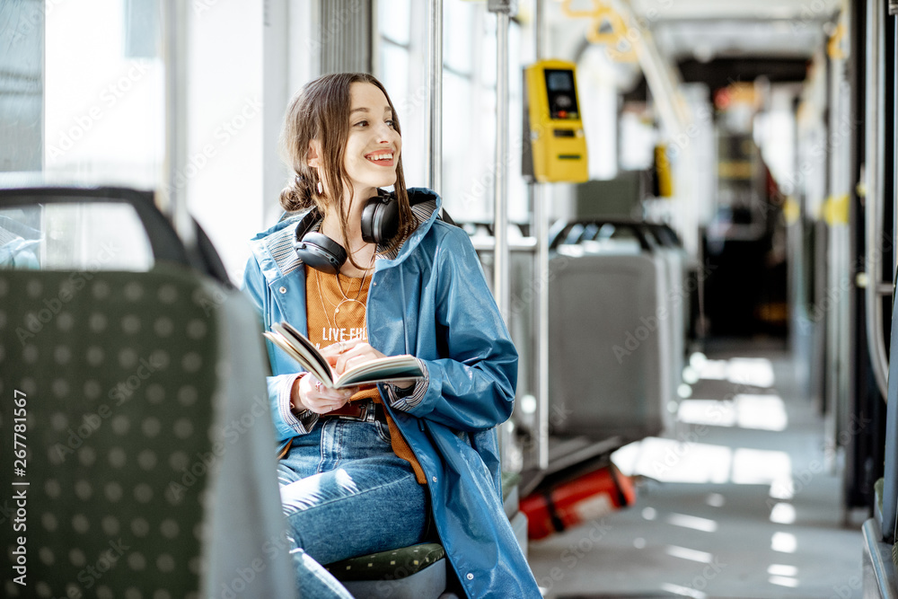 Young woman reading book while moving in the modern tram, happy passenger at the public transport