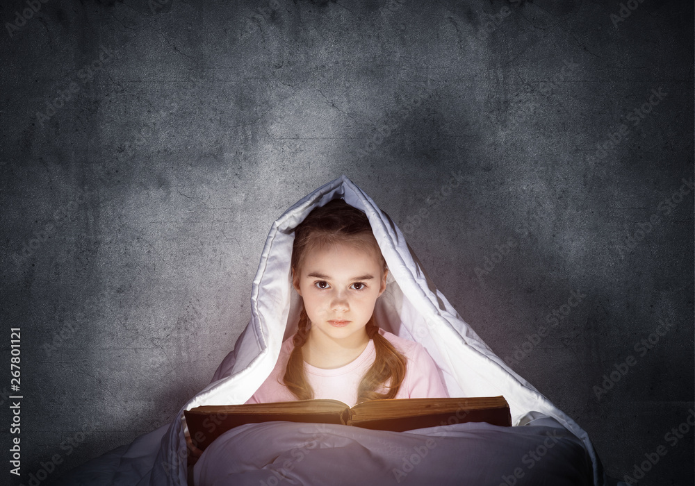 Little girl reading book in bed