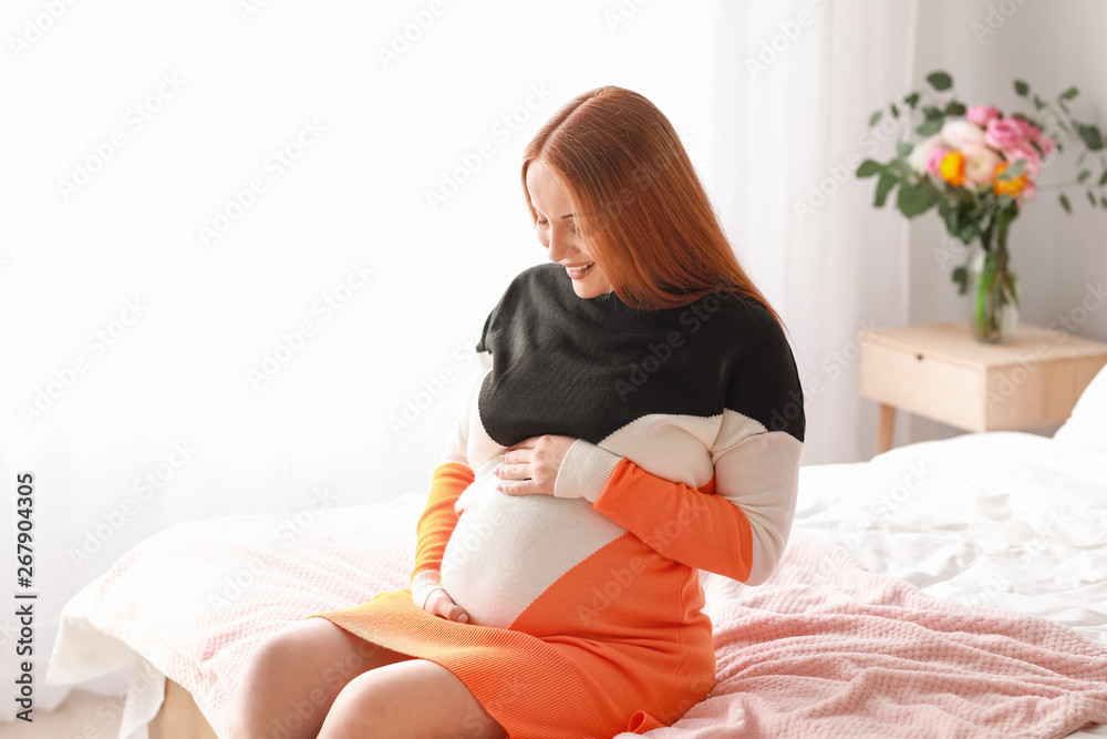 Beautiful pregnant woman sitting on bed at home