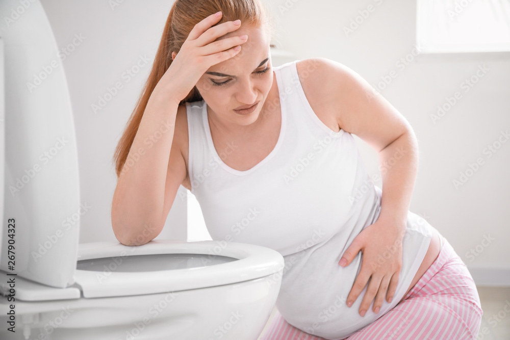 Young pregnant woman suffering from toxicosis in restroom