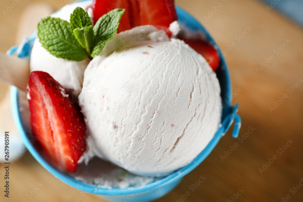 Bucket with tasty ice cream and strawberry on table, closeup