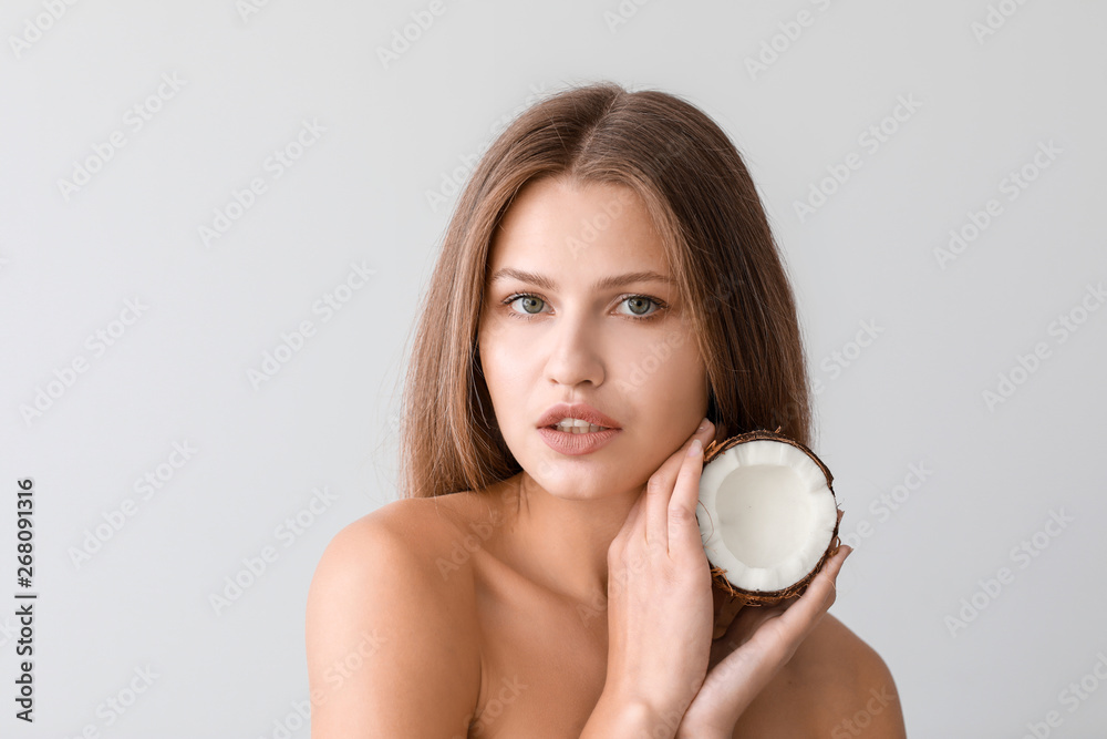 Beautiful young woman with coconut on light background