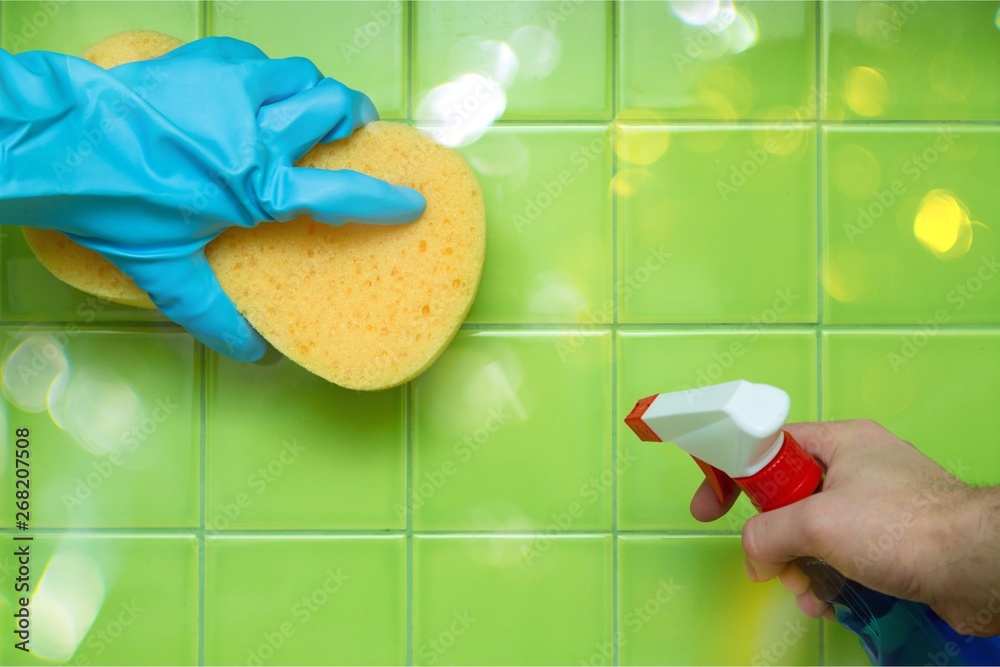 Lef Hand in Rubber Glove Holding an Yellow Sponge and Cleaning Tiles, Right Hand Holding a Spray Bot