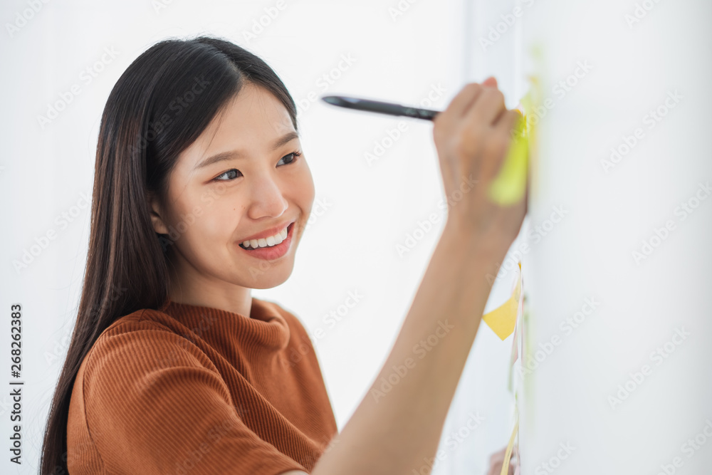 Young Asian business woman writing on sticky note for reminder list and pending works