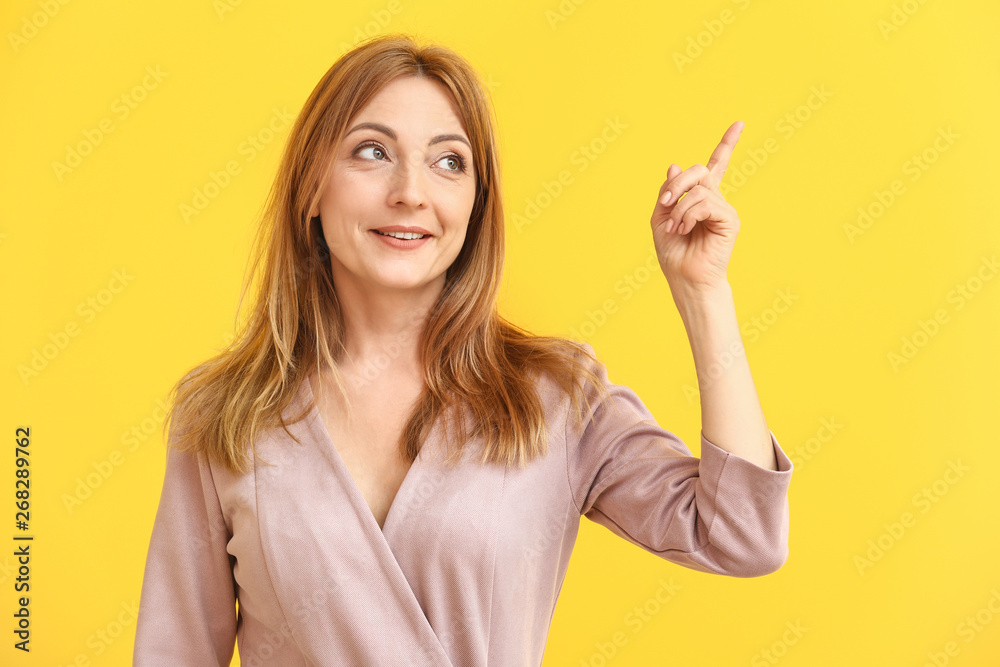 Portrait of mature woman pointing at something on color background