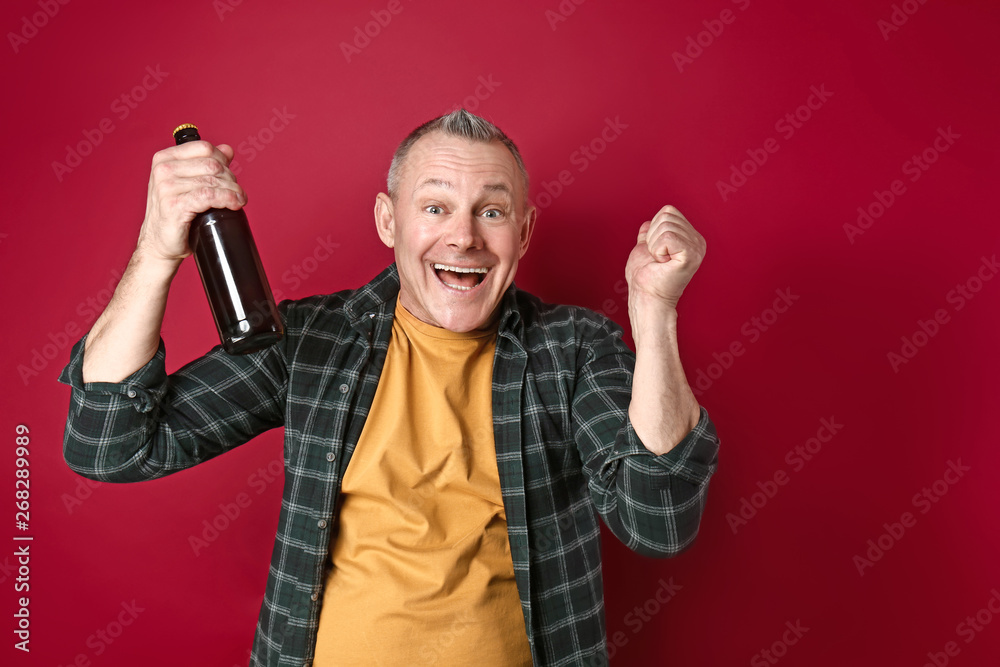 Happy middle-aged man with bottle of beer on color background