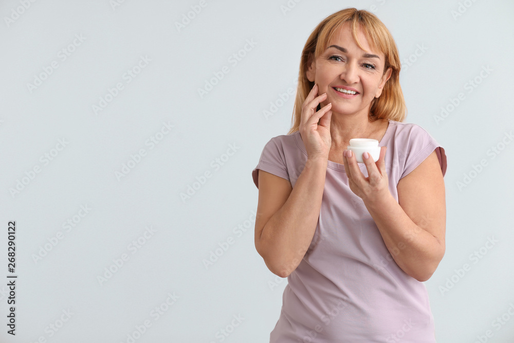 Mature woman with jar of cream on color background