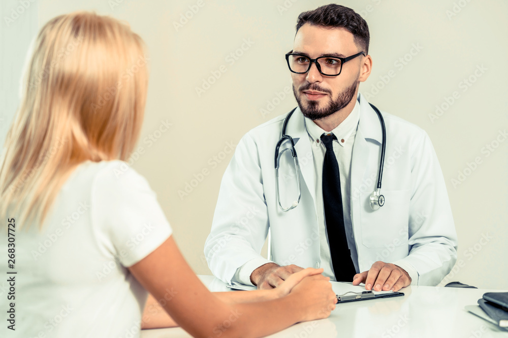 Male doctor is talking to female patient in hospital office. Healthcare and medical service.