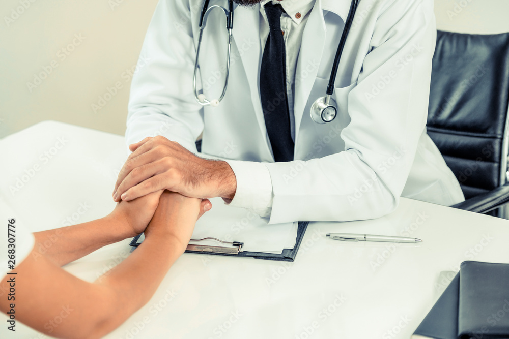 Male doctor soothes a female patient in hospital office while holding the patients hands. Healthcare