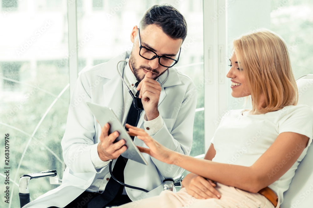 Male doctor and female patient looks at tablet computer for health data record. Healthcare and medic