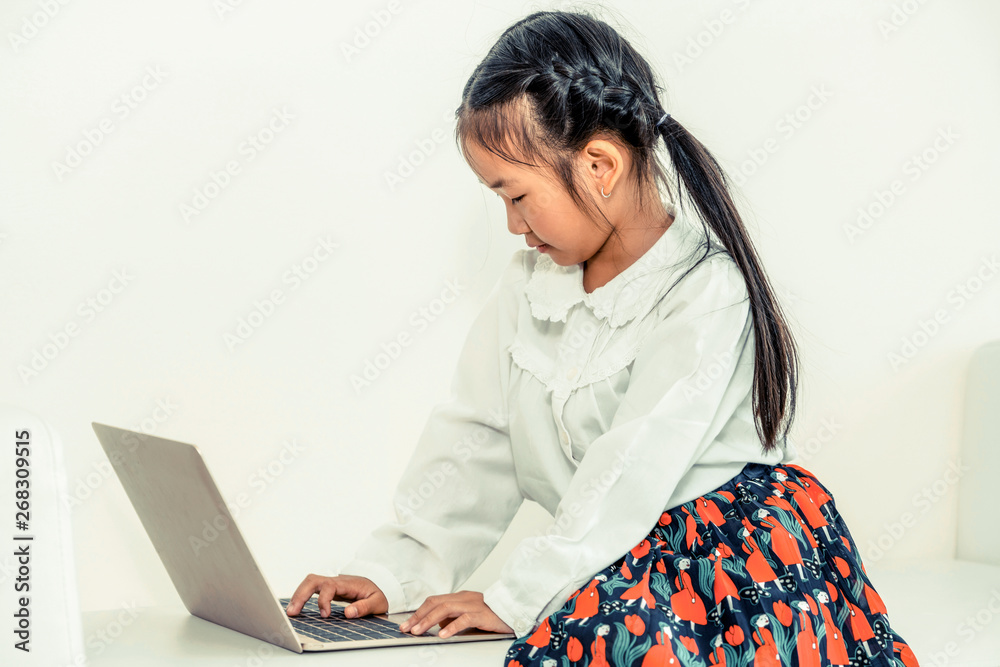 Little happy kid using laptop computer sitting on white sofa. Childhood lifestyle.