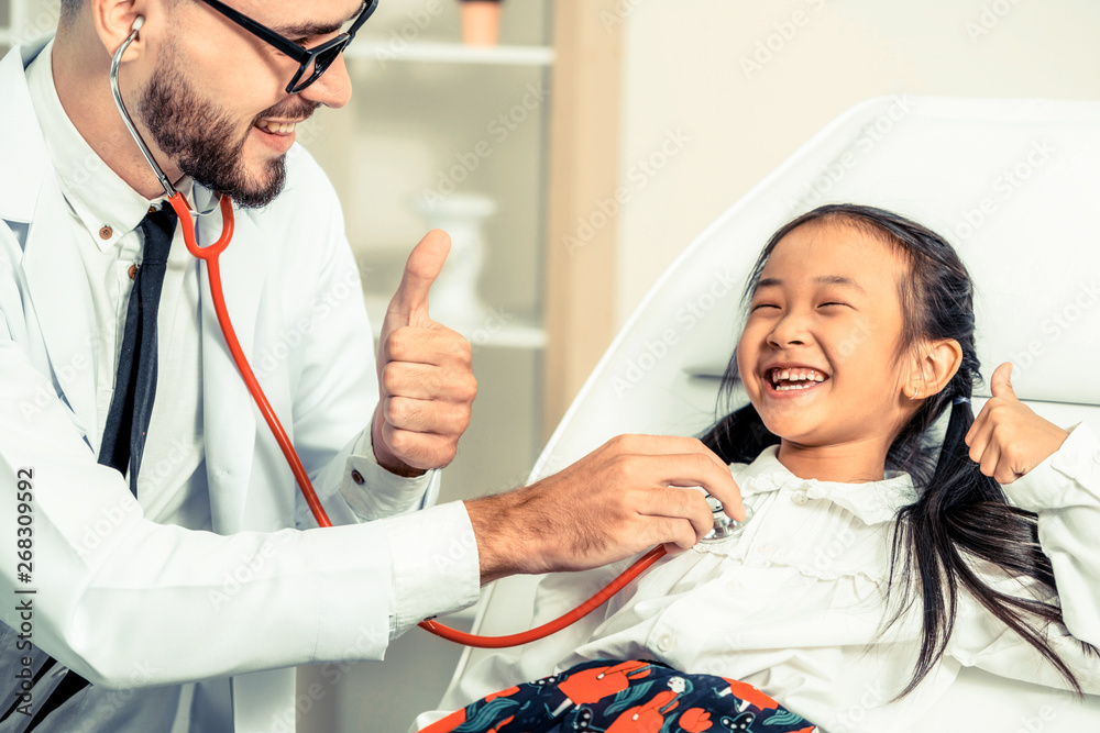 Young male doctor examining little kid in hospital office. The kid is happy and not afraid of the do