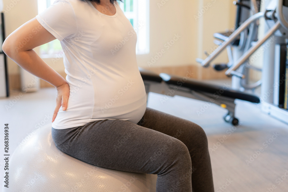 Active pregnant woman exercise in fitness center at yoga room. The young expecting mother holding ba