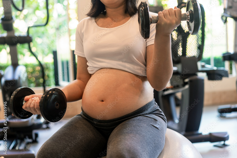 Active pregnant woman exercise in fitness center at yoga room. The young expecting mother holding ba