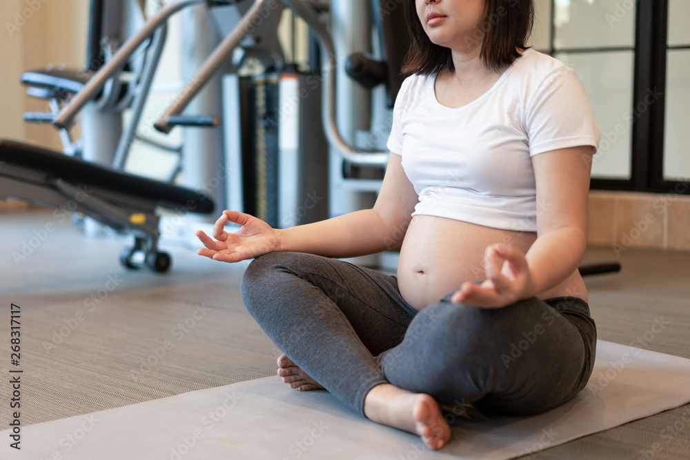 Active pregnant woman exercise in fitness center at yoga room. The young expecting mother holding ba