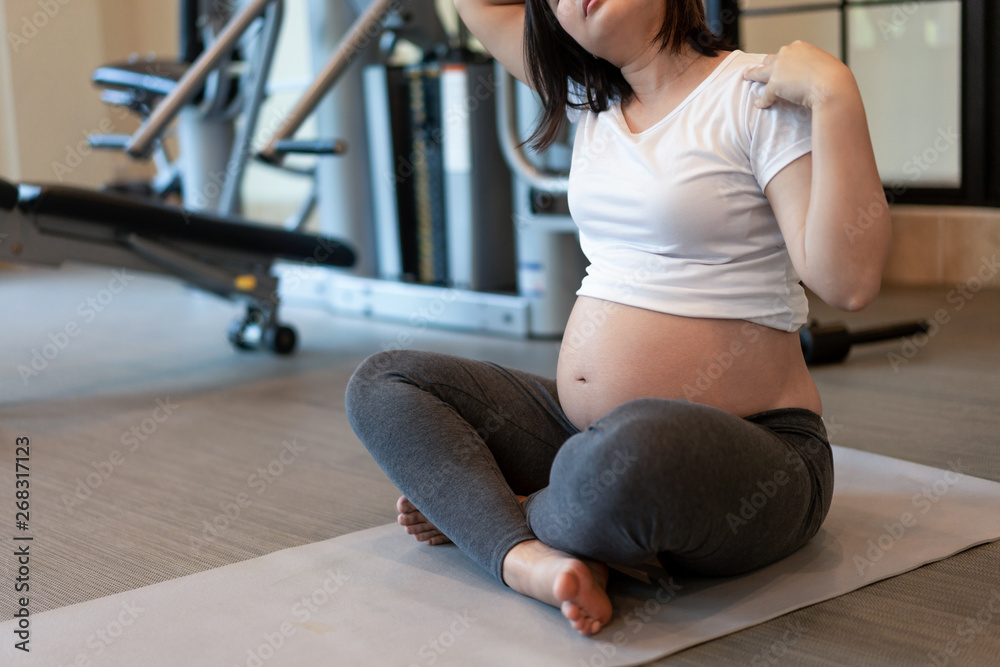 Active pregnant woman exercise in fitness center at yoga room. The young expecting mother holding ba