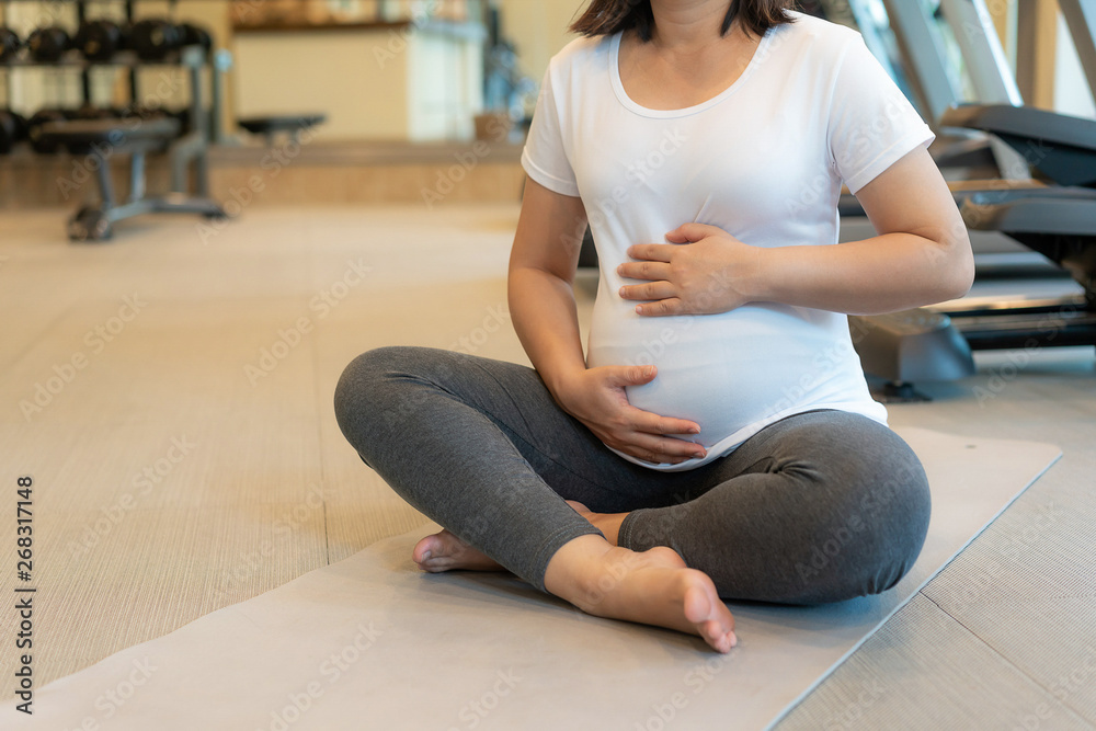 Active pregnant woman exercise in fitness center at yoga room. The young expecting mother holding ba