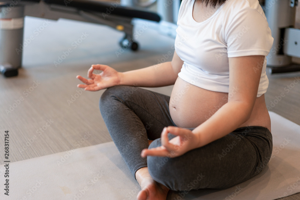 Active pregnant woman exercise in fitness center at yoga room. The young expecting mother holding ba