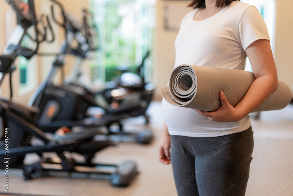 Active pregnant woman exercise in fitness center at yoga room. The young expecting mother holding ba