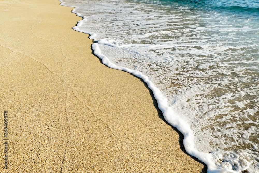 阳光明媚的日子里，沙滩岸边的海水泡沫俯视图。平静的蔚蓝海水和海洋风光