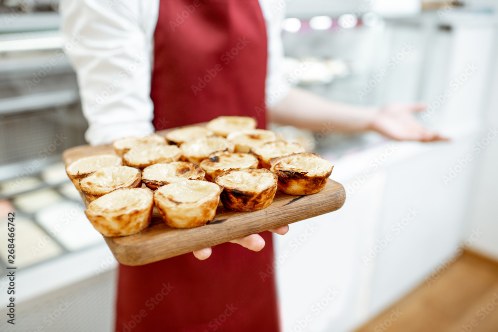 Confectioner holding fresh baked pastels de nata at the pastry shop, close-up